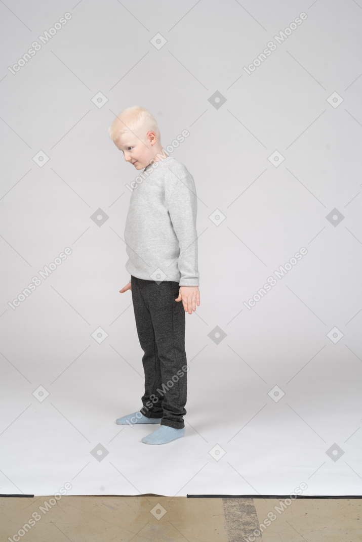 Vista de três quartos de um menino de pé com a cabeça baixa