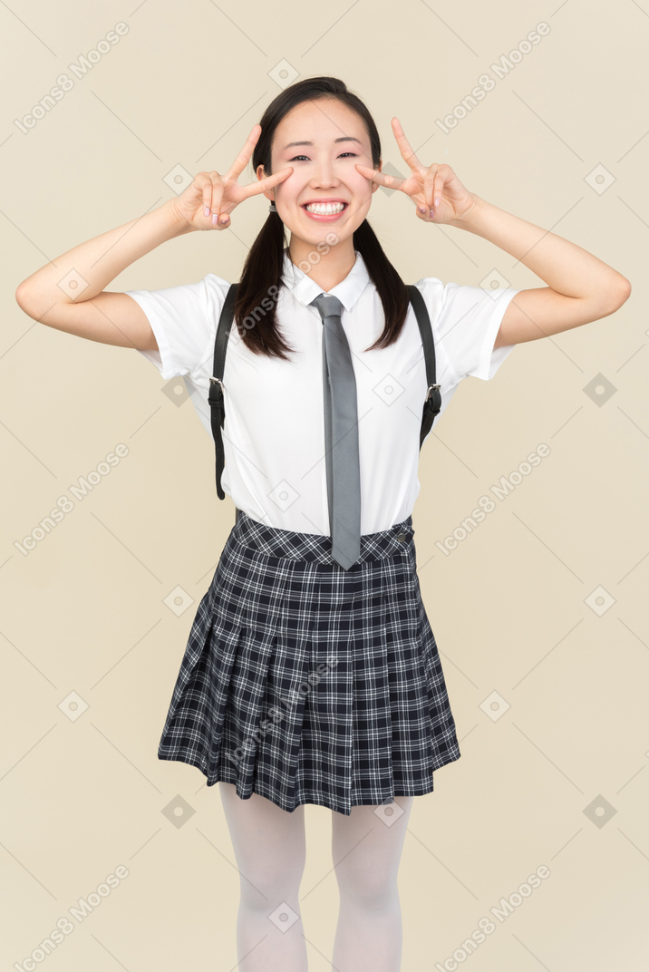 Menina da escola asiática mostrando sinal de v com ambas as mãos