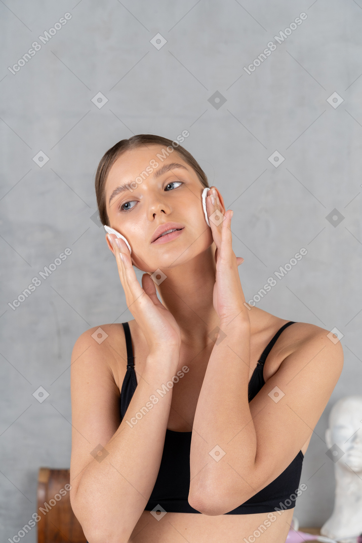 Bella giovane donna che si pulisce il viso con tamponi di cotone