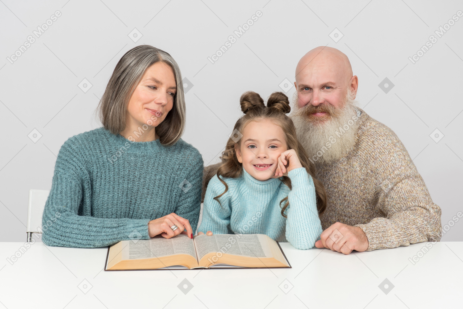 Grandparents and kid girl granddaughter sitting at the table with open book