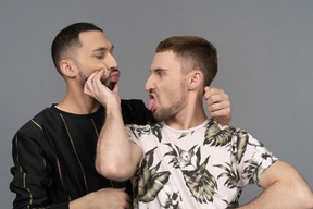 Portrait of a young caucasian man fooling around and poking another's cheeks