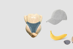 Whole raw chicken in panties, banana, baseball cap and sunglasses on gray background
