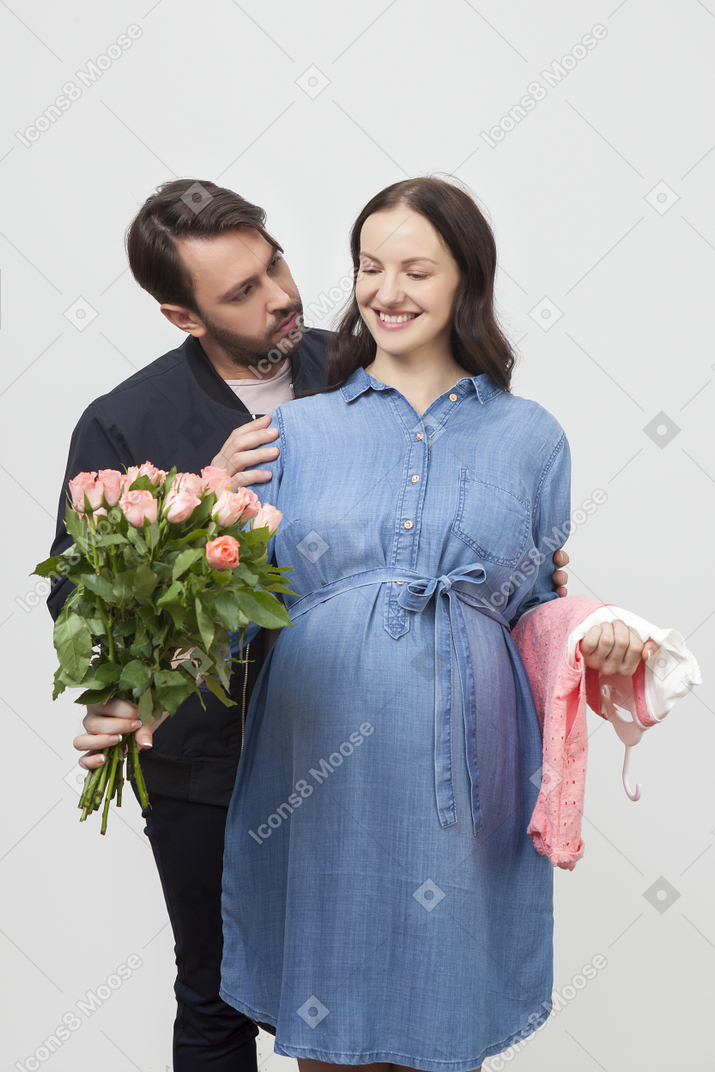 妊娠中の女性を後ろから抱きしめ、ピンクのバラを渡す男性
