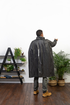 Vista posterior de un hombre con impermeable atrapando gotas de lluvia en una taza