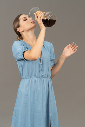 Three-quarter view of a young woman in blue dress drinking wine out of a pitcher