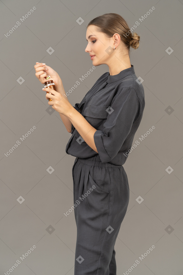 Side view of a young woman in a jumpsuit looking at the pills in a jar
