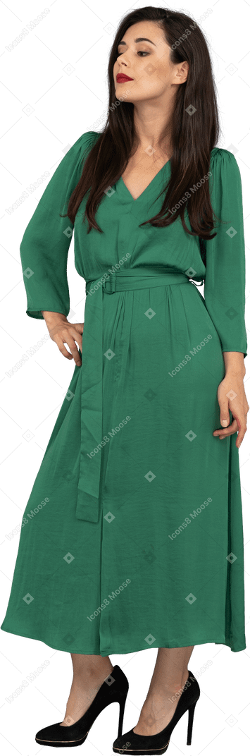 腰に手を置いている緑のドレスを着た誇り高き若い女性の4分の3のビュー