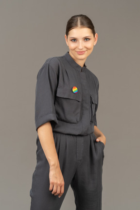 Front view of a young woman in a jumpsuit with lgbt pin putting hand in pocket