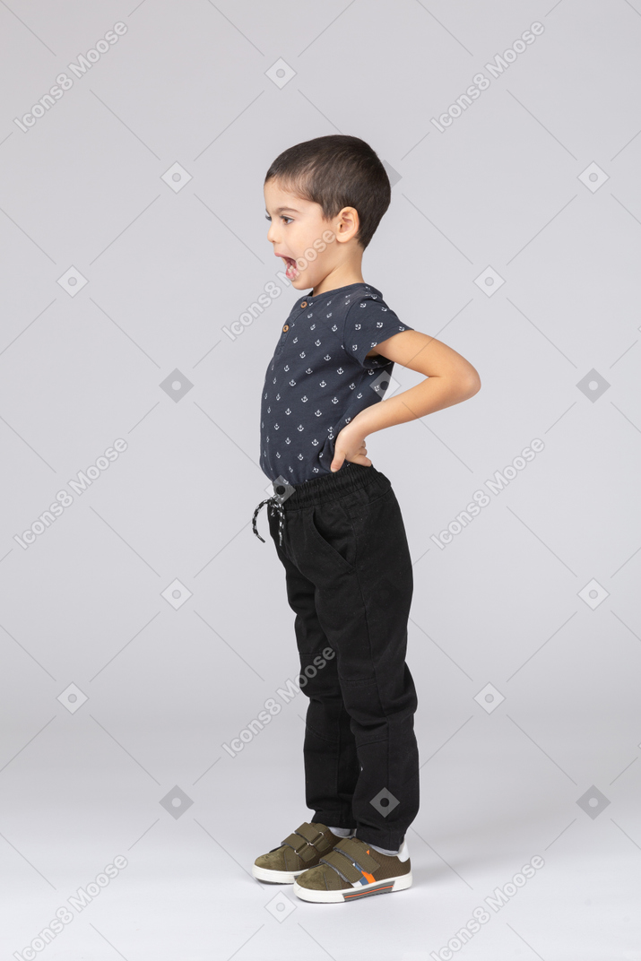 Side view of a cute kid boy standing with hands on hips