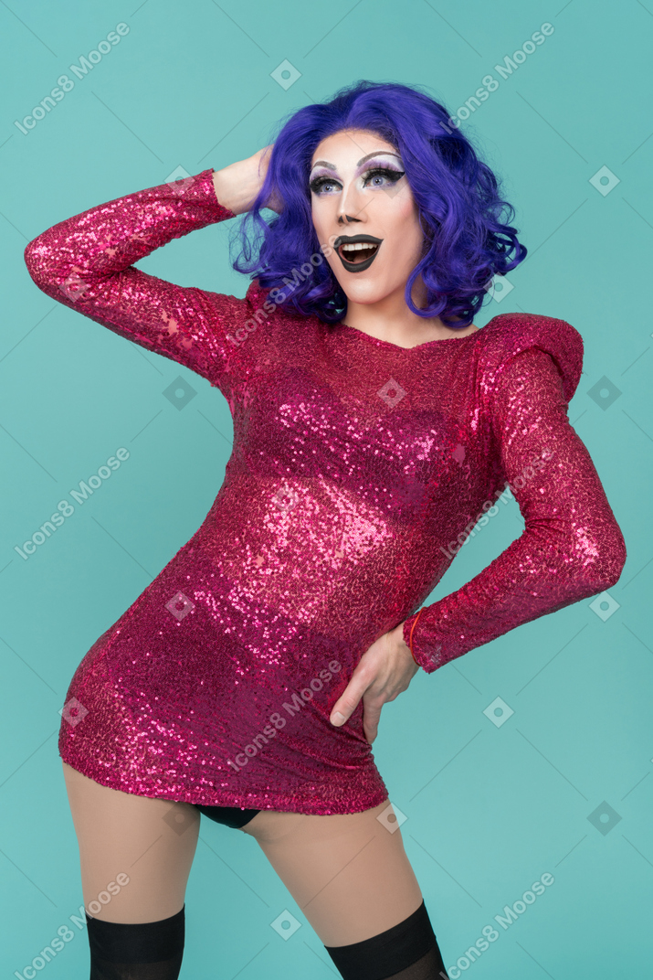 Drag queen looking excited while posing with one hand on hip & the other behind head