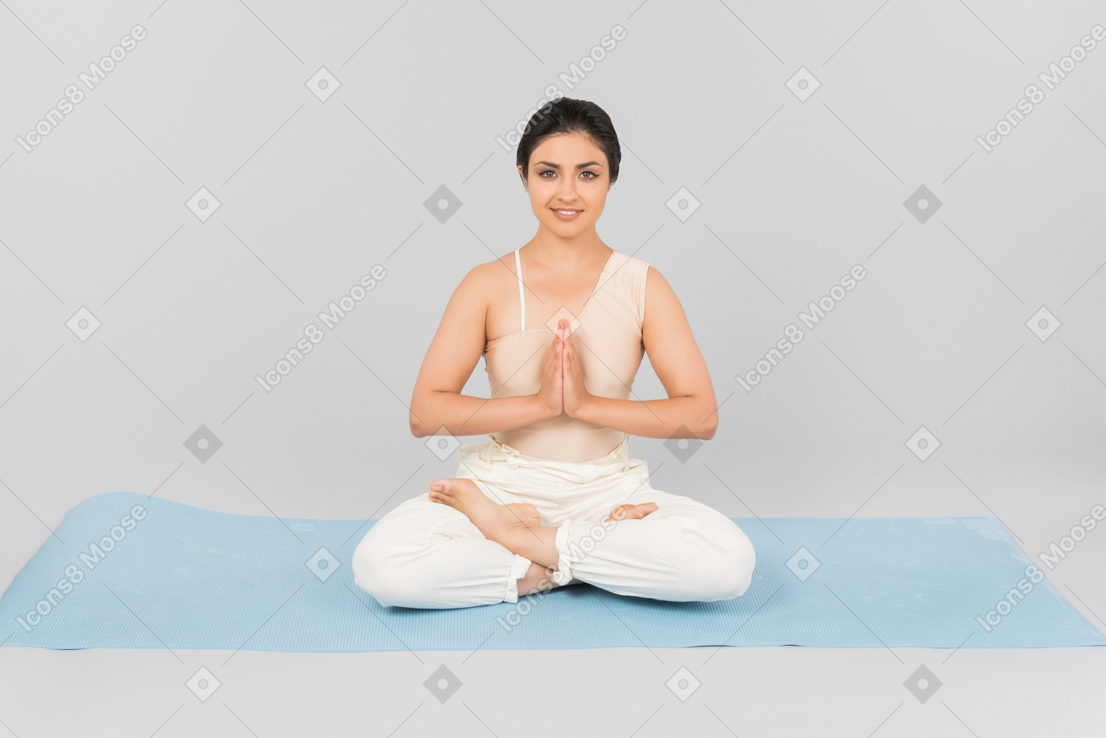 Jeune femme indienne avec les jambes croisées et les mains jointes assis sur un tapis de yoga