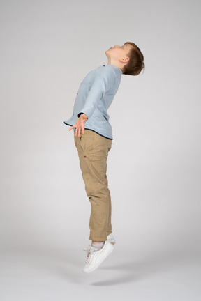 Side view of a boy jumping with his arms outstretched and looking up