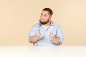 Большой человек сидит за столом и держит зубную пасту и зубную щетку