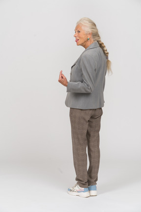 Vista traseira de uma senhora idosa de terno apontando para cima com um dedo