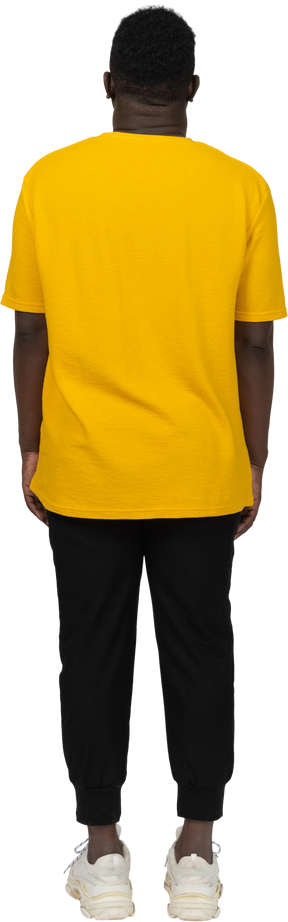 노란색 티셔츠를 입은 어두운 피부의 젊은 남자가 가만히 서 있는 뒷모습