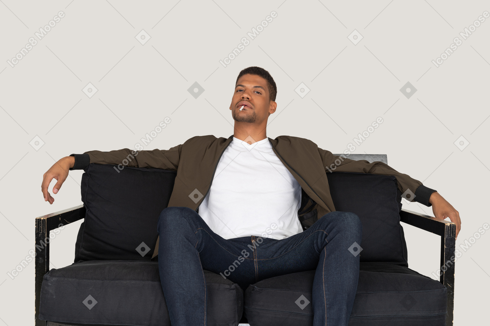 Vista frontal del joven sentado en un sofá y sosteniendo el cigarrillo en la boca