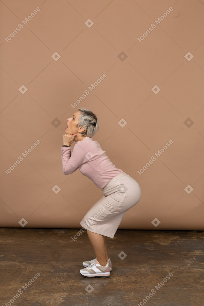 Vista lateral de una mujer en ropa casual en cuclillas y haciendo muecas