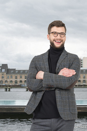 A man with a beard and glasses standing in front of a body of water