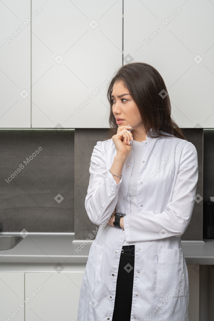 Front view of a  suspicious female doctor touching chin and looking aside