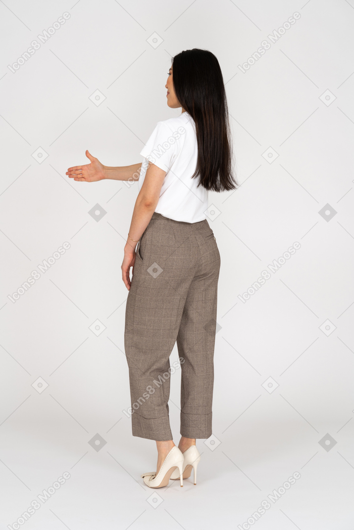 Dreiviertel-rückansicht einer grüßenden jungen dame in reithose und t-shirt, die ihre hand ausstreckt