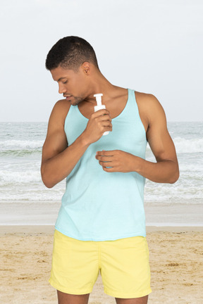 A man standing on a beach holding sunscreen