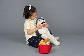 Retrato de una niña alimentando a un perro de peluche