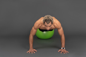 Front view of a shirtless afro man making push-ups on a gym ball