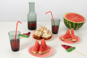 A table full of summertime snacks and drinks, along with some cute mini-cakes for a birthday celebration on a hot summer day