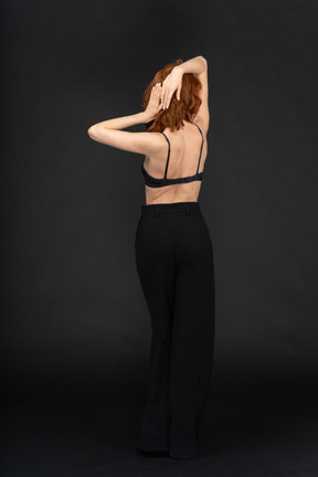 A back side view of the young sexy woman on the black background touching her hair