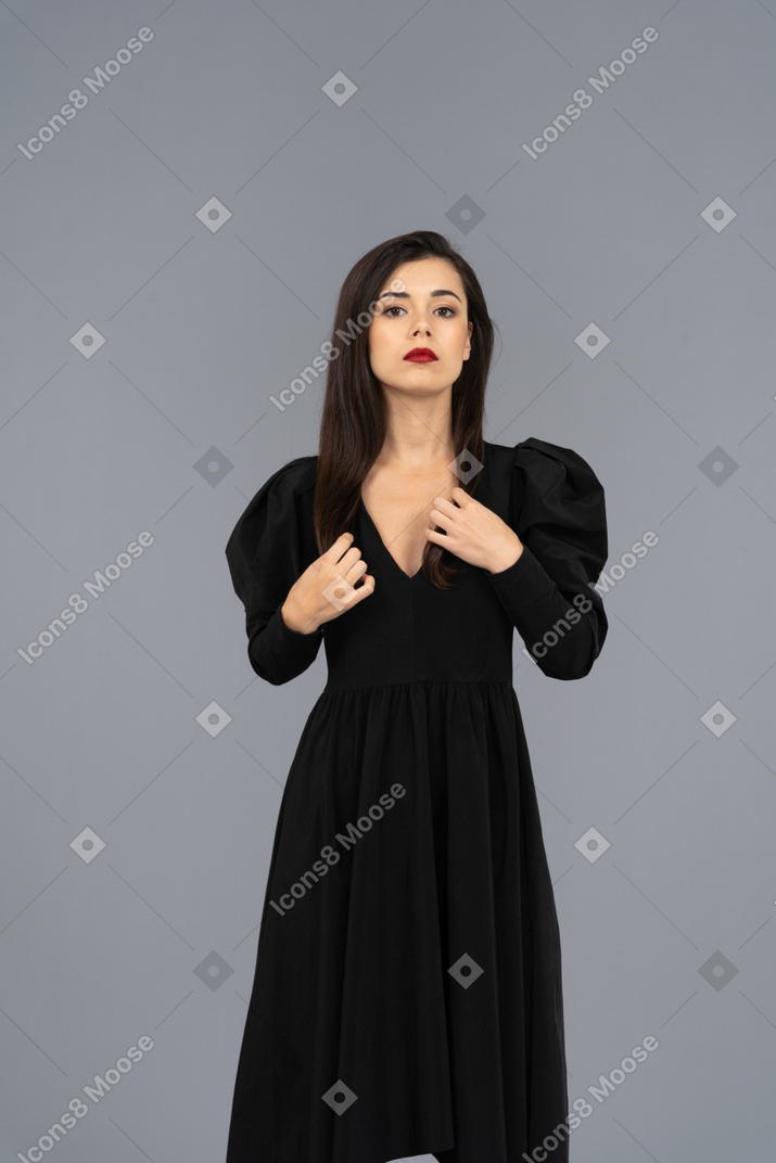 Вид спереди серьезной молодой женщины, поправляющей свое черное платье