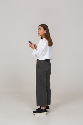 Vista lateral de uma jovem com roupas de escritório, verificando o feed por telefone