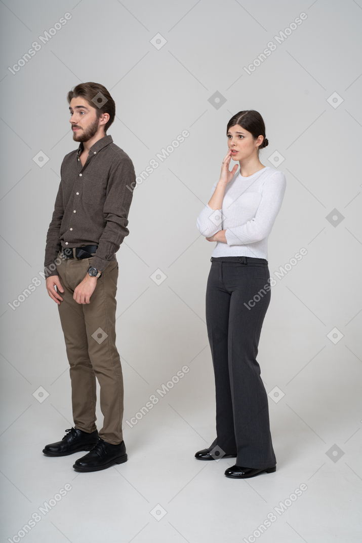 Vista de tres cuartos de una pareja joven perpleja en ropa de oficina