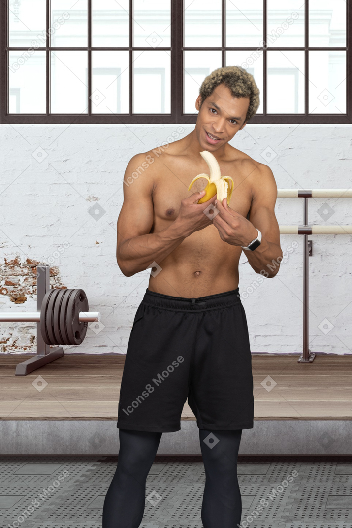 A topless sportsman holding a banana at a gym
