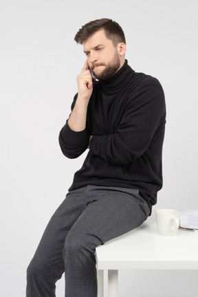 Frown office worker sitting on white desk and talking on the phone