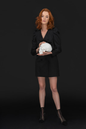 A frontal view of the sexy elegant woman holding a skull and looking to the camera