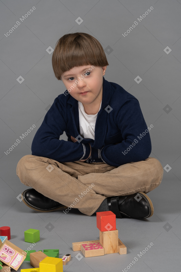 Kleiner junge, der gelangweilt aussieht, während er neben seinem spielzeug sitzt