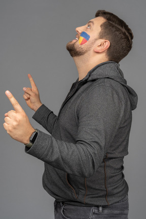 Side view of a male football fan with colorful face art raising fingers