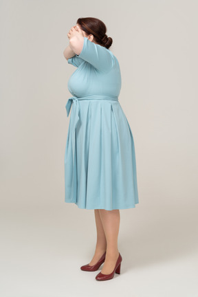 Вид сбоку на женщину в голубом платье, закрывающую глаза руками