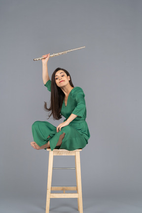 Dreiviertelansicht einer verrückten klarinettenspielerin, die mit gekreuzten beinen auf einem stuhl sitzt