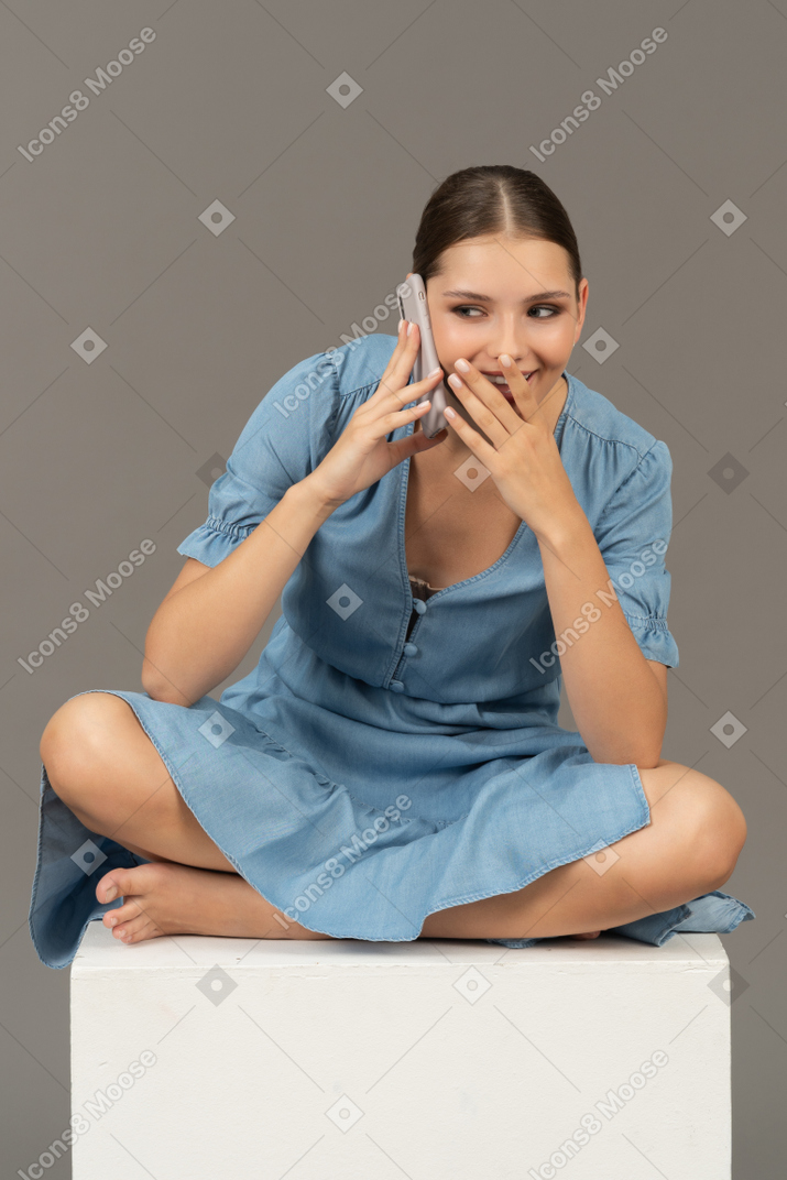 立方体に座ってスマートフォンで話している若い女性の正面図