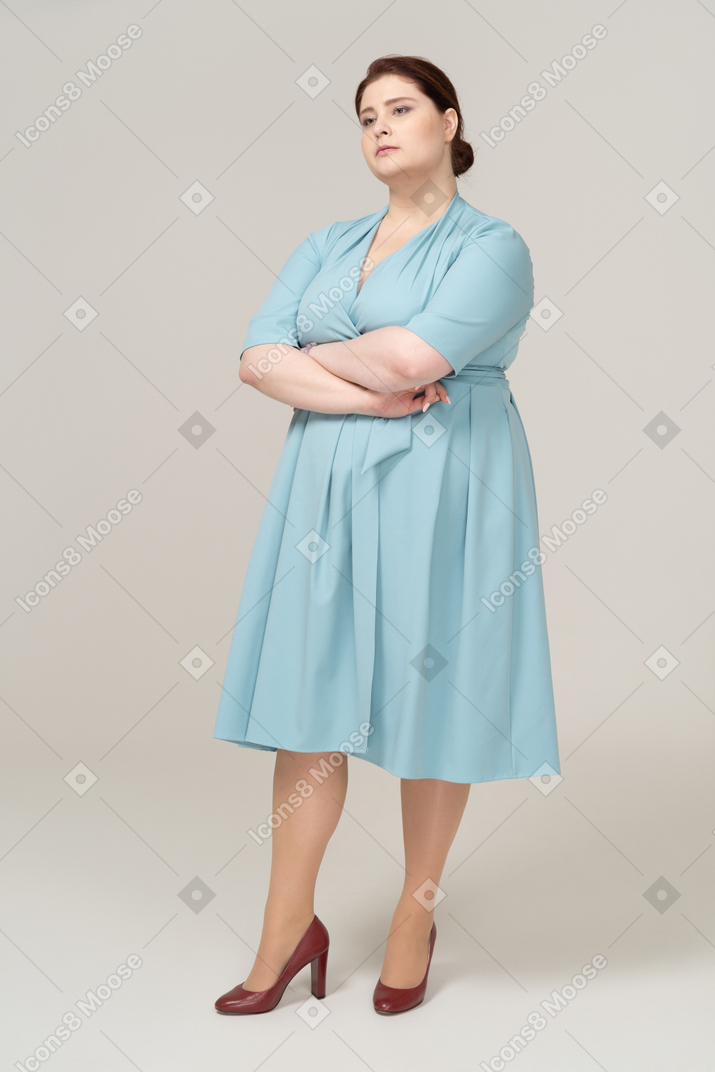 Vista lateral de uma mulher de vestido azul posando com os braços cruzados