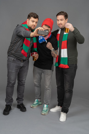 Vista frontal de tres aficionados al fútbol masculino tomando selfie