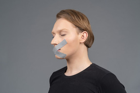 Three-quarter view of person with duct tape on mouth and eyes closed