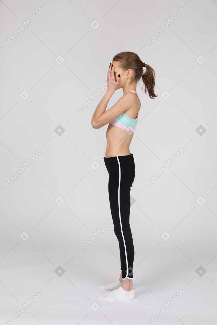 Vista lateral de uma adolescente em roupas esportivas escondendo o rosto