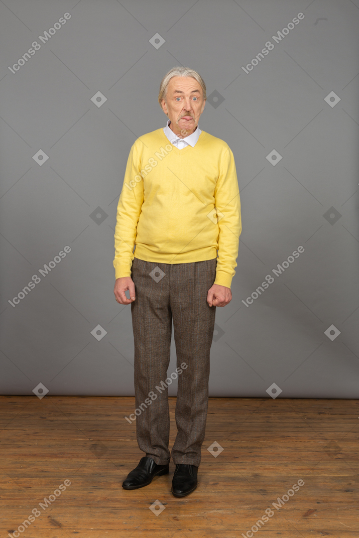 舌を示す黄色のプルオーバーの老人の正面図