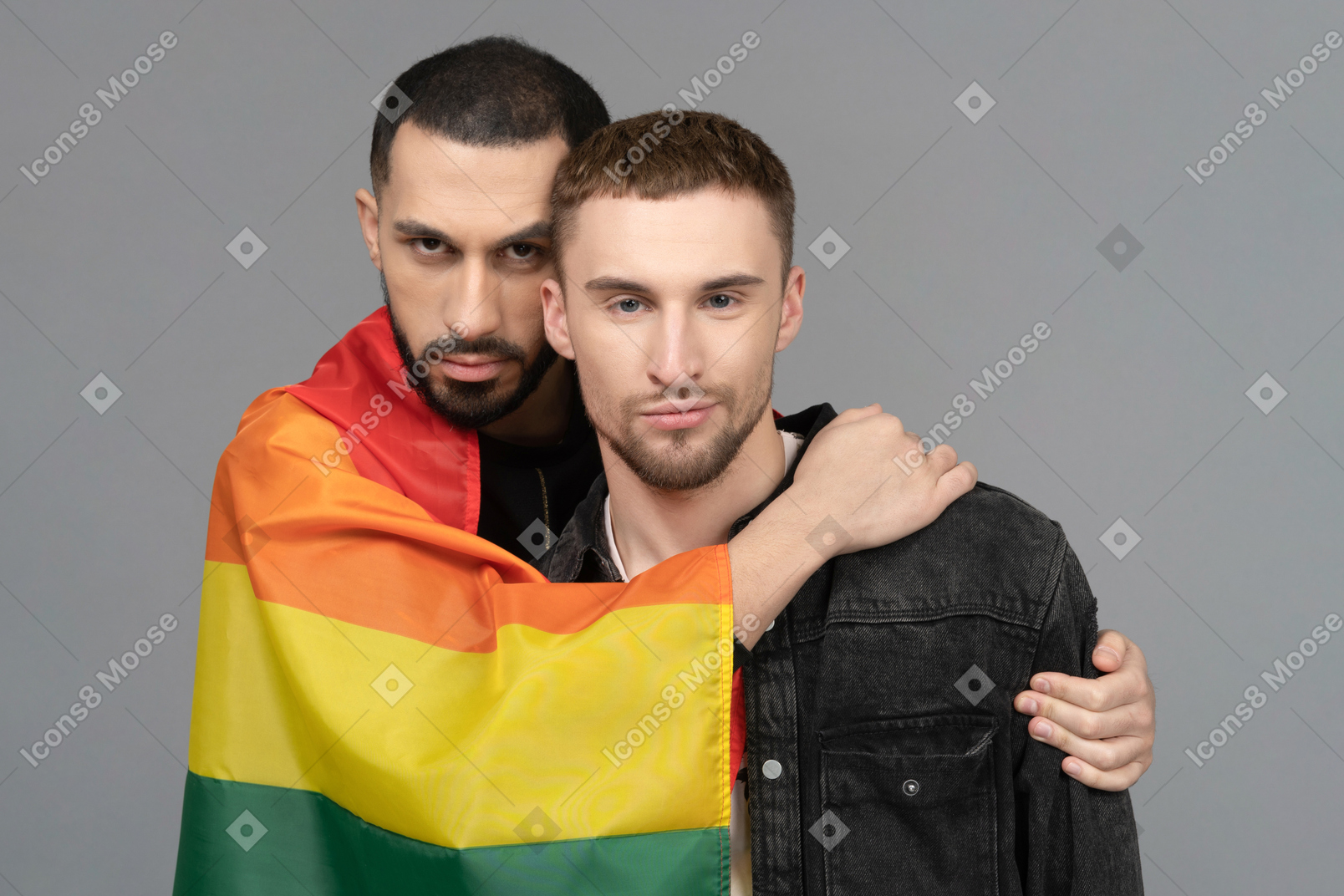 Front view of two young men half-hugging while wearing lgbt flag