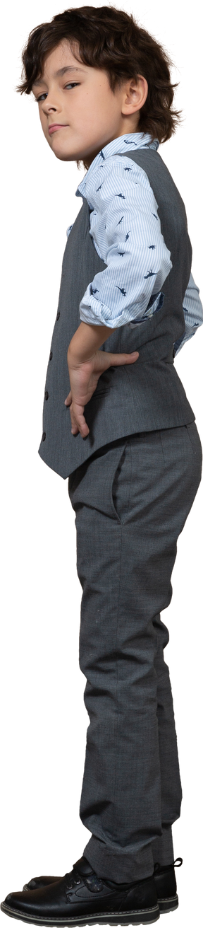 Vista lateral de un chico lindo con traje gris posando con las manos en las caderas