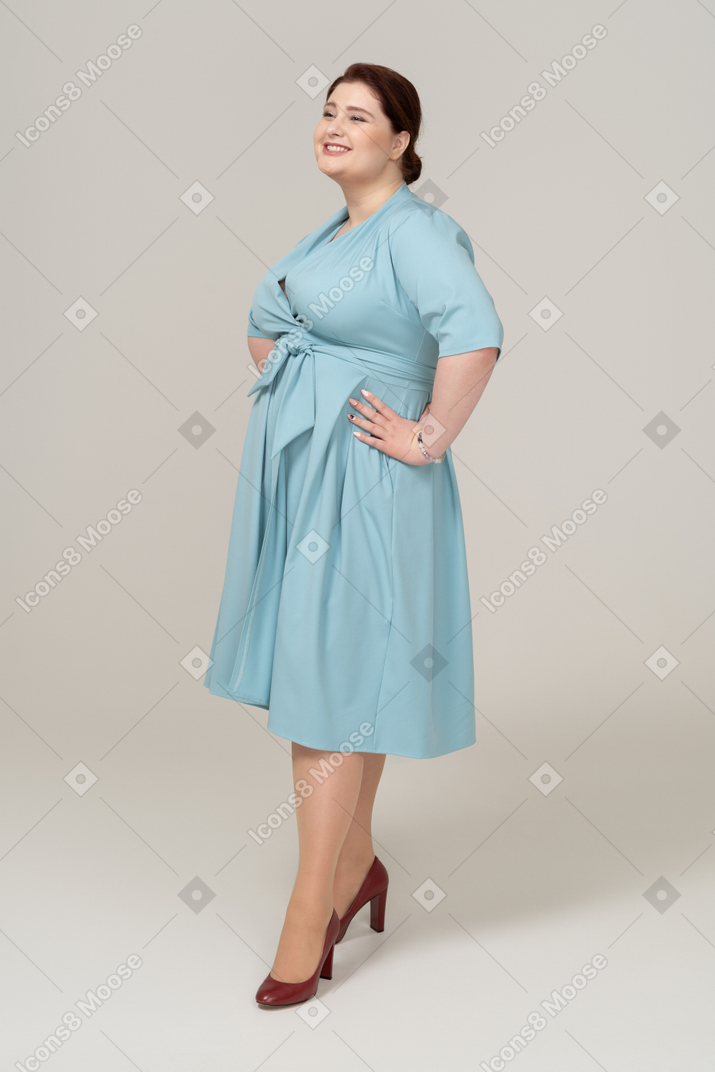 一个穿着蓝色连衣裙的快乐女人双手叉腰站立的侧视图