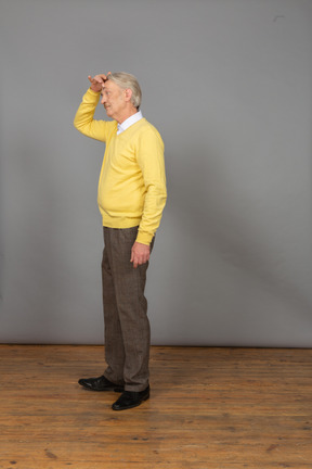 Vista de três quartos de um velho confuso tocando a cabeça e vestindo um pulôver amarelo