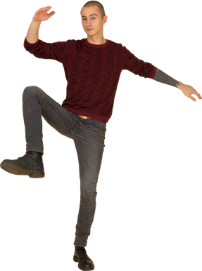 Front view of a balancing young man in red pullover raising hands